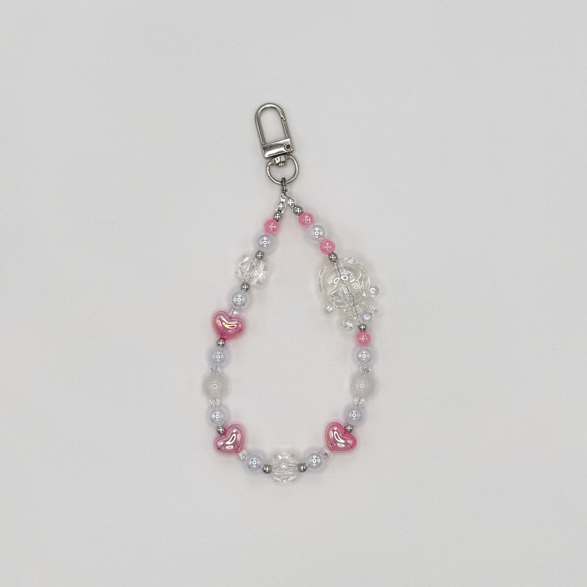 Phone wrist strap with pink heart-shaped beads, frosted white round beads, clear crystal bicone beads, and silver spacers, featuring a clear transparent character charm, on a silver swivel clasp."\