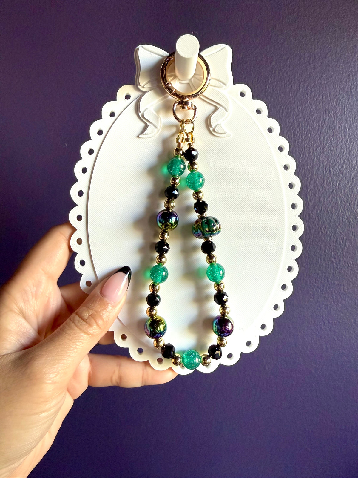 Green and black beaded wristlet keychain with a dark green jack-o’-lantern bead, iridescent round beads, and gold-tone accents.