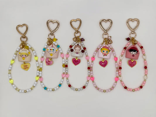 Five kawaii phone charm keychains displayed in a row on a white background, each featuring a different chibi figure peeking out of a pastel envelope with a heart enamel charm and gold heart-shaped clasp. Variants include Sweet Bean, Pucky, SP, Molly, and Haci, each with a unique color-coordinated beaded loop strand.