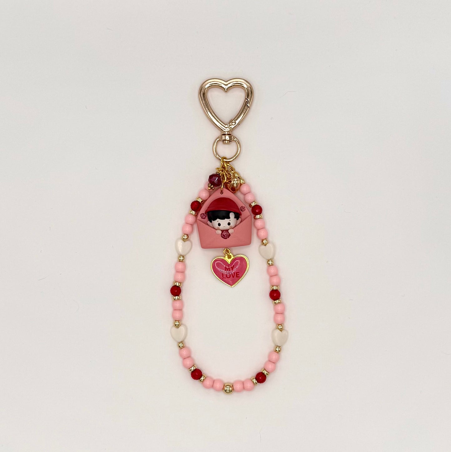 Kawaii phone charm keychain featuring a Haci chibi figure peeking out of a pink envelope, with a 'My Love' heart enamel charm, gold heart-shaped clasp, and a beaded loop strand of pink, cream, and red beads with gold accents.