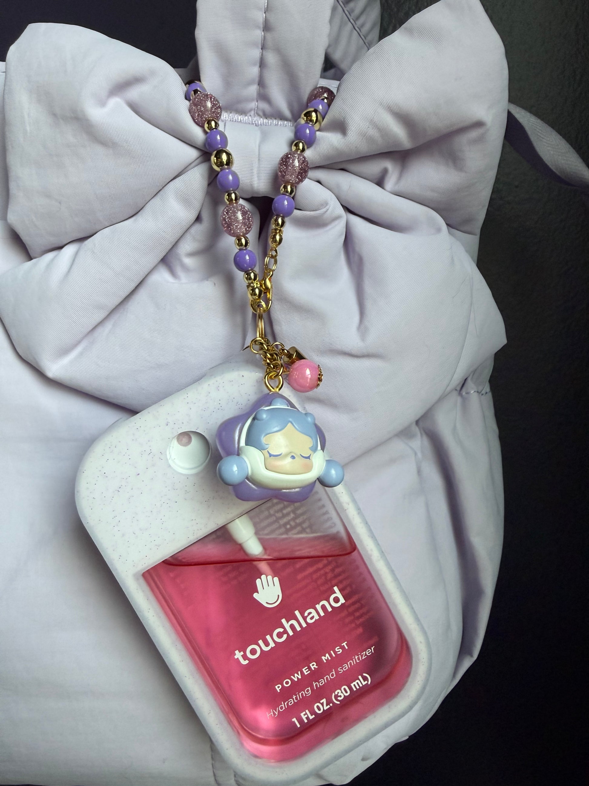 Touchland Power Mist hand sanitizer in a white glitter silicone case on a white background. Attached gold lobster clasp keychain features a red-cloaked SP chibi charm with a round face, paired with a beaded wrist strap of alternating red and silver glitter beads with gold accent beads. TOUCHLAND NOT INCLUDED WITH THIS PRODUCT!