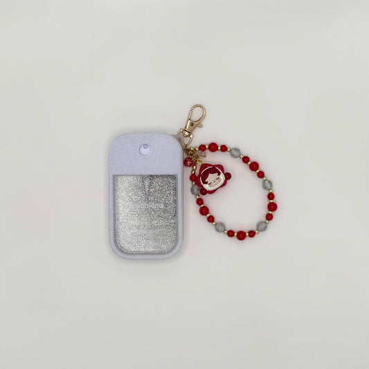 Touchland Power Mist hand sanitizer in a blush pink silicone case with a glitter window on a white background. Attached gold lobster clasp keychain features a Skullpanda chibi charm in a pink hood holding a small item, paired with a beaded wrist strap of pink, orange, and gold star-shaped beads. TOUCHLAND NOT INCLUDED WITH THIS PRODUCT!