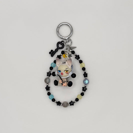 Beaded keychain with black star beads, light blue and yellow round frosted beads, and silver spacers, featuring a white cat character figure holding an axe, with a black heart key charm, silver spike charm, and star charm on a silver ring clasp