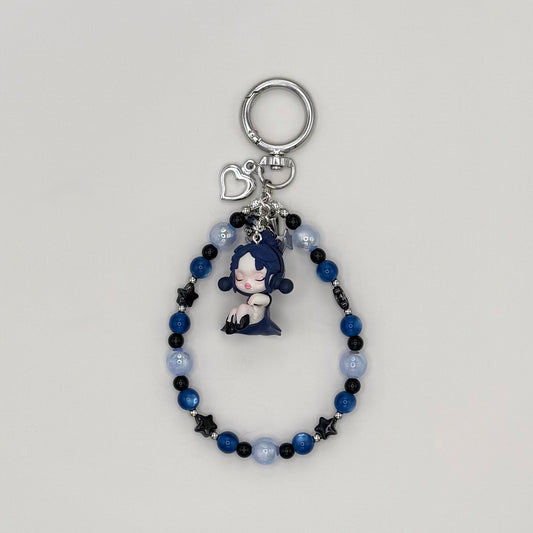 Beaded keychain with deep blue cat eye, pale blue frosted, and black star beads with silver spacers, featuring a dark blue-haired character girl figure in a navy dress, with a silver heart charm and small star charm on a silver ring clasp.