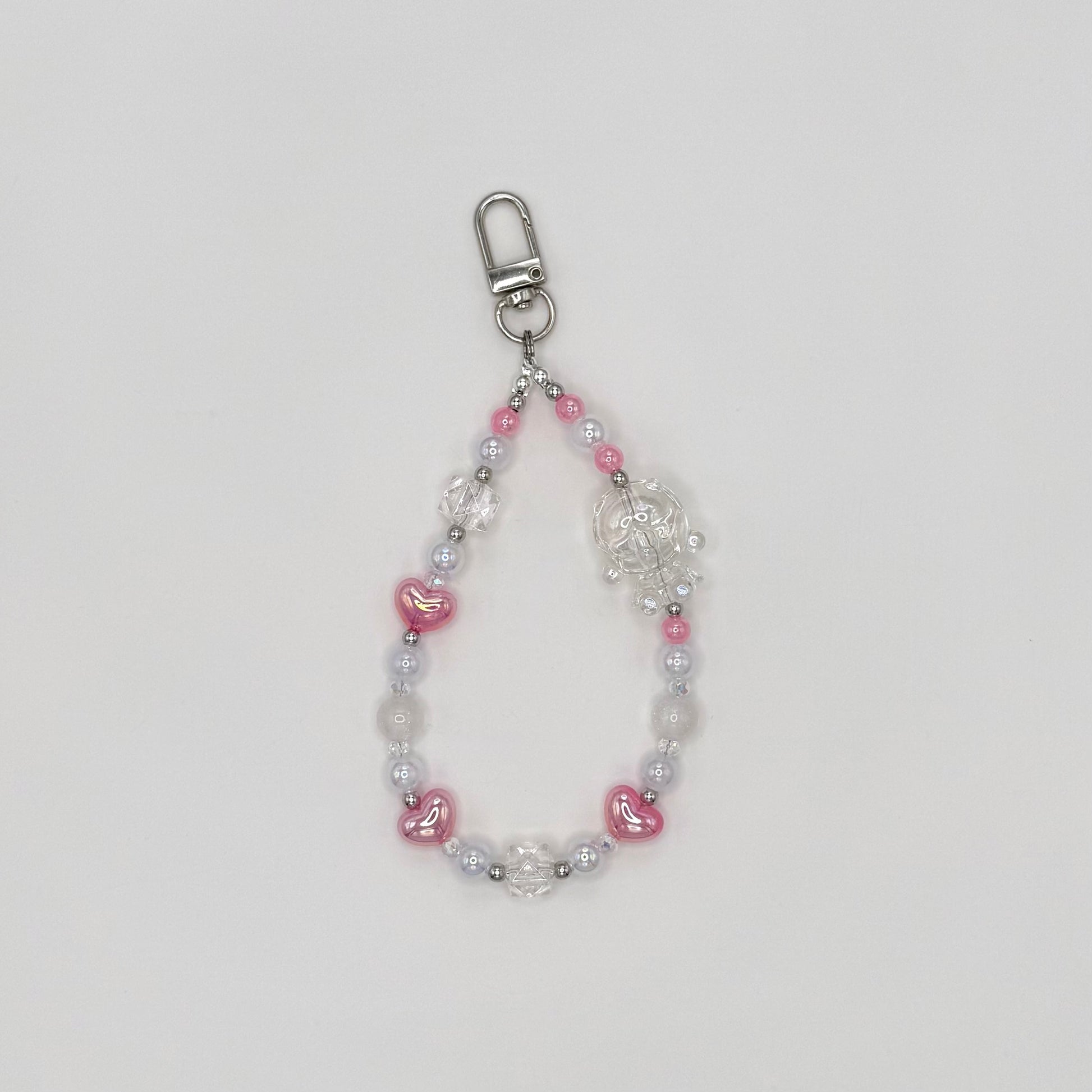 Phone wrist strap with pink heart-shaped beads, frosted white round beads, clear crystal bicone beads, and silver spacers, featuring a clear transparent character charm, on a silver swivel clasp."\