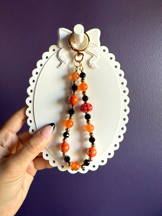 Orange and black beaded wristlet keychain with an orange jack-o’-lantern bead, glossy round beads, and gold-tone accents.