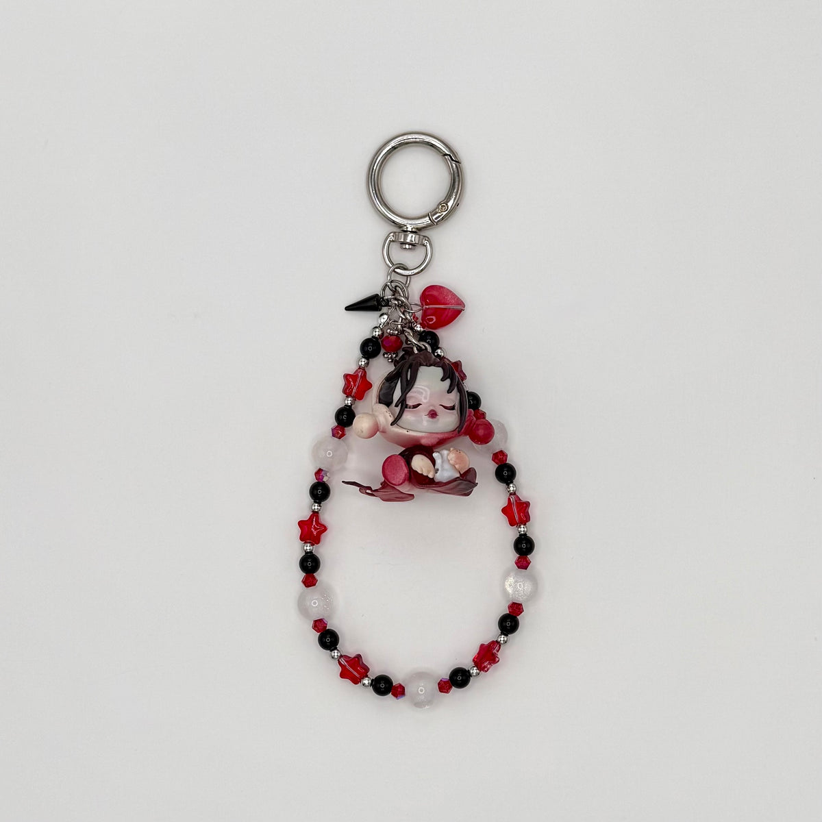 Beaded keychain with red crystal star beads, black, frosted white round beads, and silver spacers, featuring a dark-haired character girl figure in a floral dress holding rose petals, with a red heart charm and silver spike charm on a silver ring clasp.