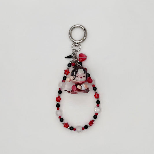 Beaded keychain with red crystal star beads, black, frosted white round beads, and silver spacers, featuring a dark-haired character girl figure in a floral dress holding rose petals, with a red heart charm and silver spike charm on a silver ring clasp.