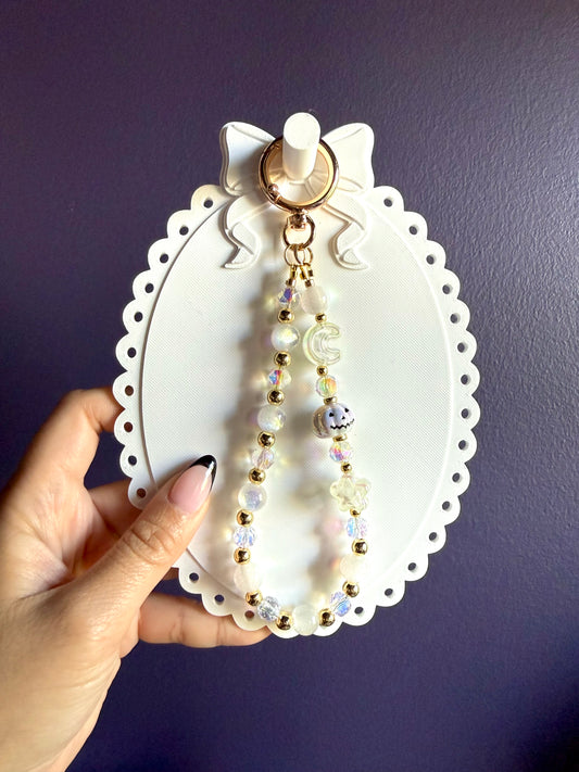 White beaded wristlet keychain with a white jack-o’-lantern bead, translucent moon and star beads, and gold-tone accents.