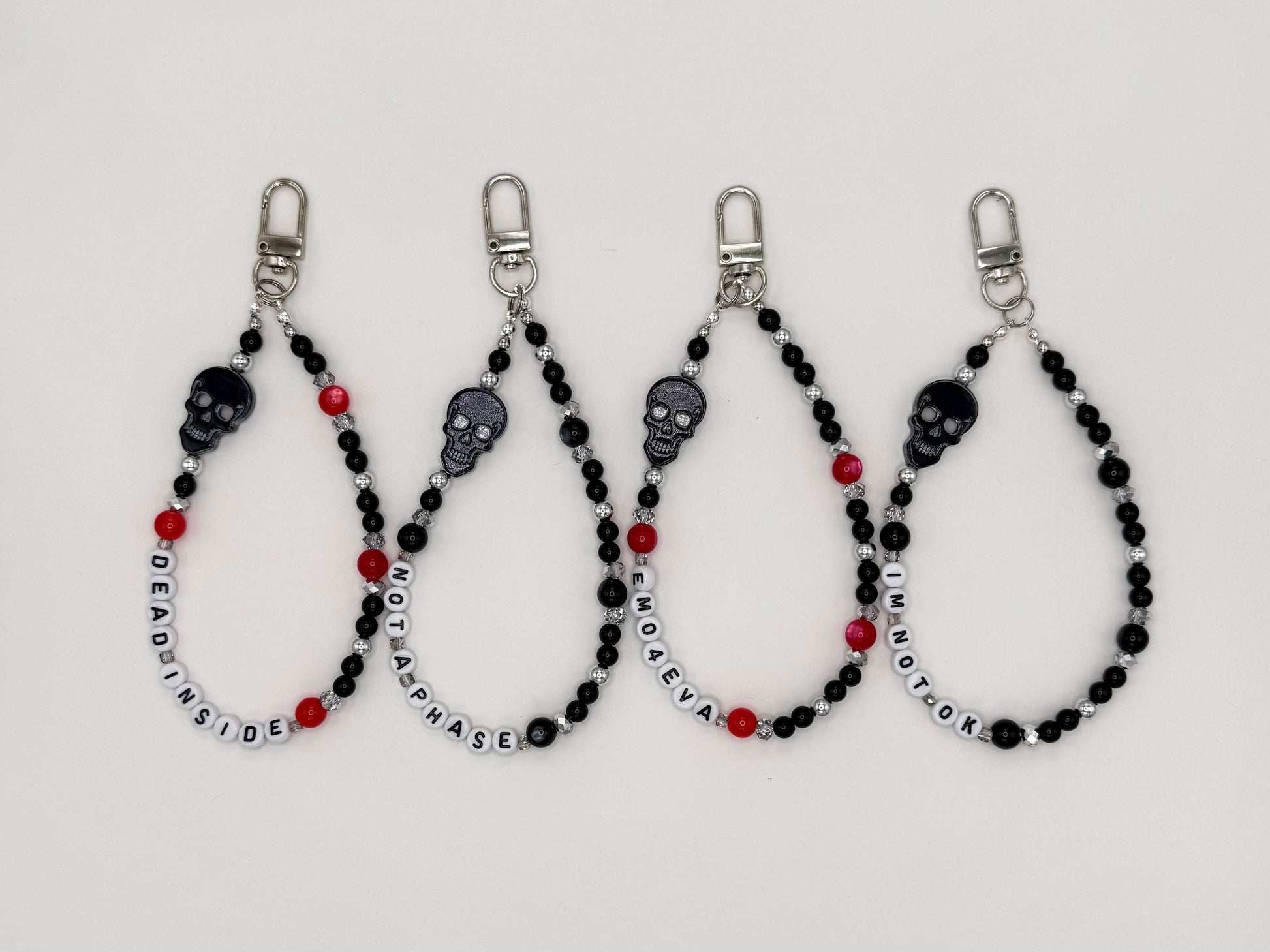 Four black beaded keychain wrist straps with skull beads and letter beads reading DEAD INSIDE, NOT A PHASE, EMO4EVA, and IM NOT OK.