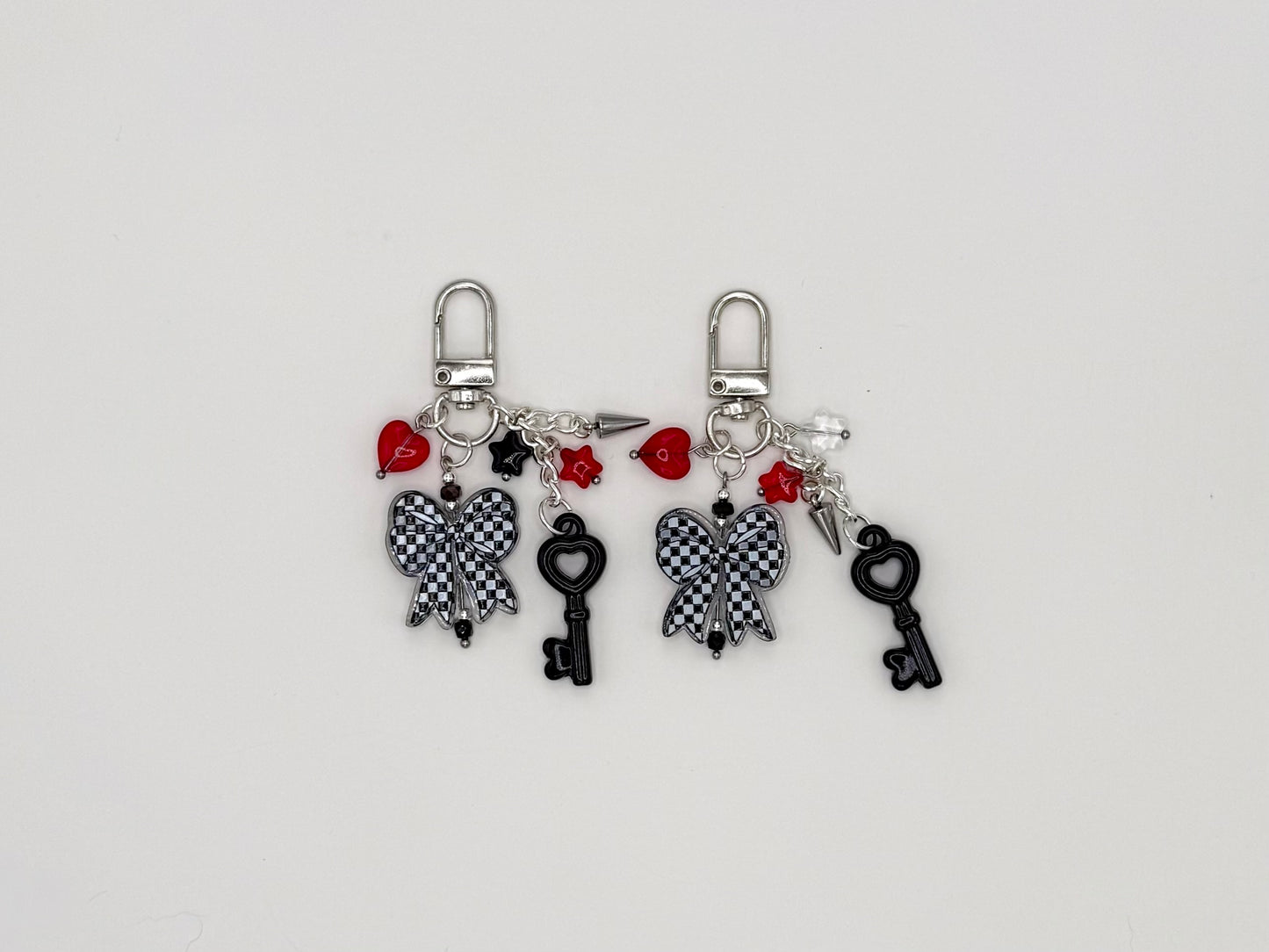 Two silver charm keychains featuring checkered bow, heart key, spike, star, and red heart charms