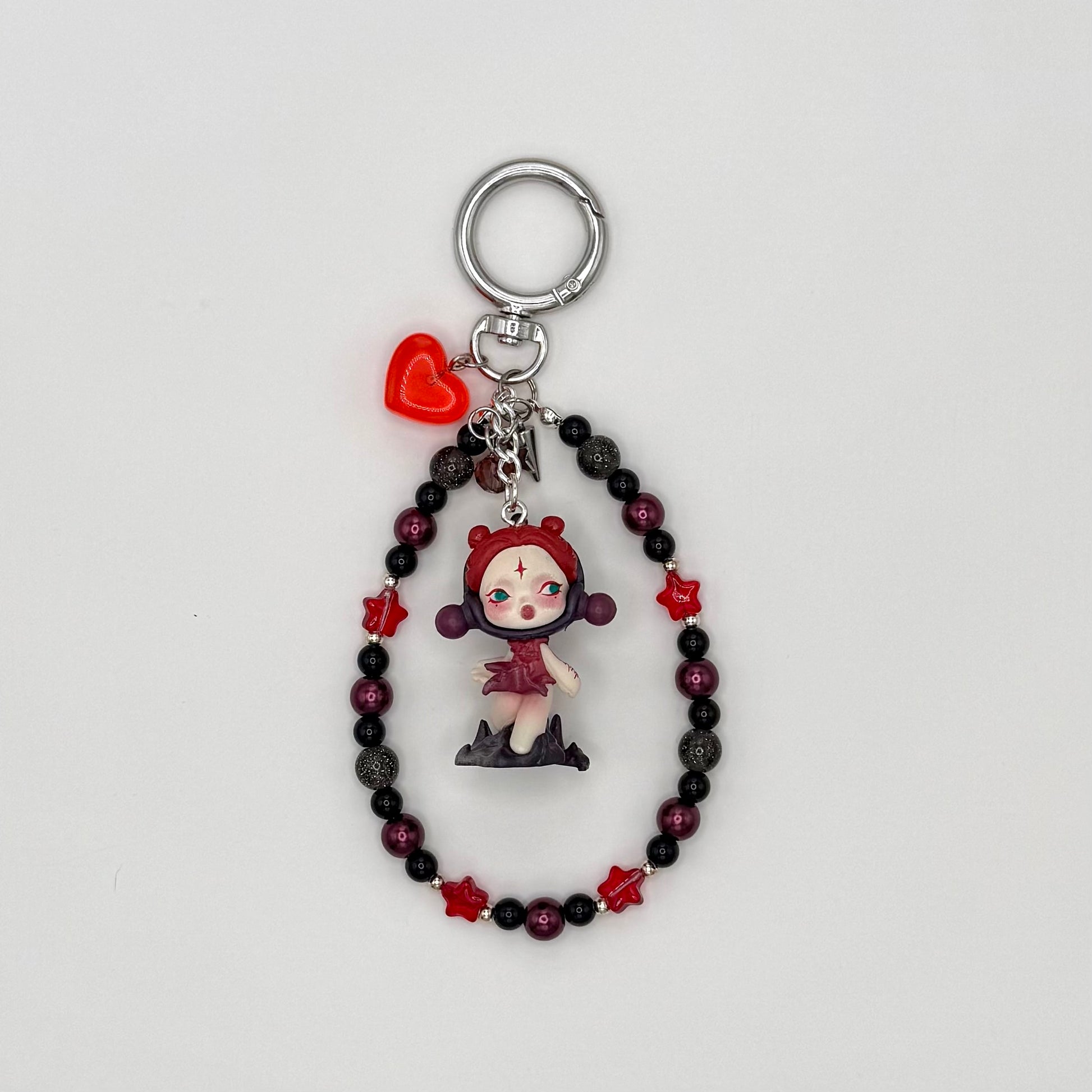 Beaded keychain with deep burgundy pearl, black acrylic, gray glitter, and red crystal star beads with silver spacers, featuring a red-hooded character figure in a dark red dress with a star on her forehead, with a red heart charm and silver spike charm on a silver ring clasp.