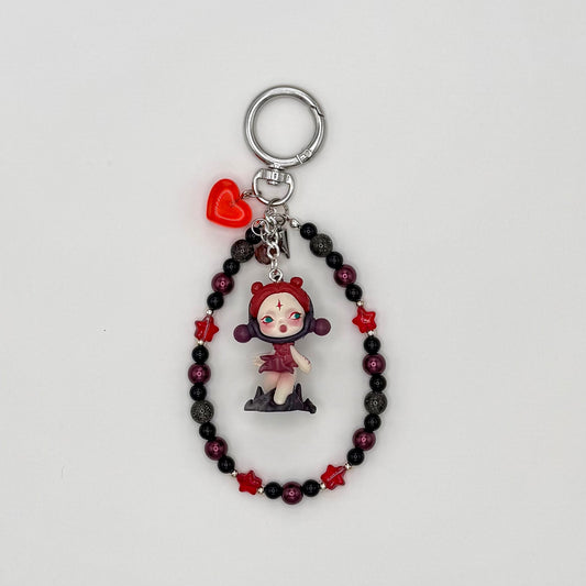 Beaded keychain with deep burgundy pearl, black acrylic, gray glitter, and red crystal star beads with silver spacers, featuring a red-hooded character figure in a dark red dress with a star on her forehead, with a red heart charm and silver spike charm on a silver ring clasp.